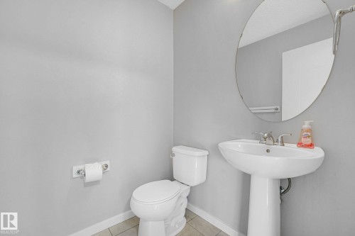 Bathroom featuring a pedestal sink with chrome faucet, a white toilet, and a large oval mirror - 17724 58 Street Nw, Edmonton, AB 