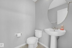 Bathroom featuring a pedestal sink with chrome faucet, a white toilet, and a large oval mirror - 