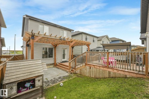 Spacious backyard featuring a multi-level wood deck with railing, an overhead pergola, a concrete patio area, and a lush green lawn - 17724 58 Street Nw, Edmonton, AB 