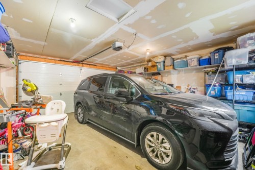 Attached garage featuring a sectional overhead door, exposed ceiling joists, and concrete flooring - 17724 58 Street Nw, Edmonton, AB 