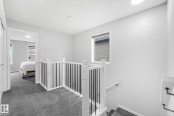 Carpeted landing featuring a white and black spindle railing, natural light from a window, and recessed lighting - 