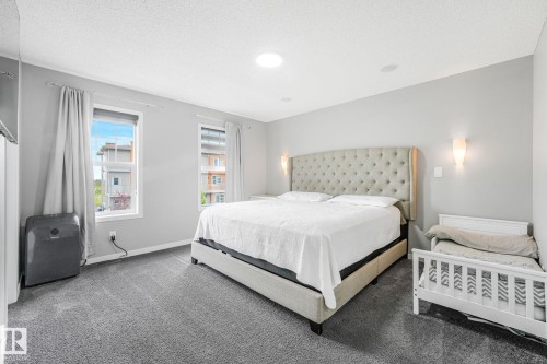 Bedroom featuring soft gray carpet flooring, two windows with white trim, and light gray wall sconces - 17724 58 Street Nw, Edmonton, AB 