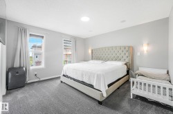 Bedroom featuring soft gray carpet flooring, two windows with white trim, and light gray wall sconces - 