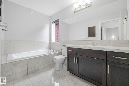 Bathroom featuring a full-size bathtub with surrounding tile, dark wood-finish vanity with an integrated sink, and an expansive wall-mounted mirror - 17724 58 Street Nw, Edmonton, AB 