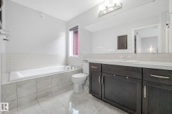 Bathroom featuring a full-size bathtub with surrounding tile, dark wood-finish vanity with an integrated sink, and an expansive wall-mounted mirror - 