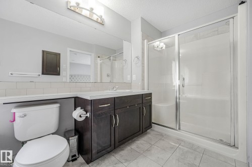 Bathroom featuring a sliding glass shower enclosure with a built-in bench, a dark wood-finish vanity with a white countertop and integrated sink, a large wall-mounted mirror, ceramic subway tile backsplash, and light gray floor tiling - 17724 58 Street Nw, Edmonton, AB 