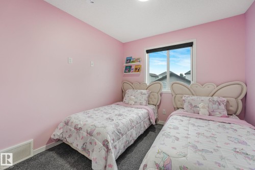 Bedroom featuring soft pink walls, dark grey carpet, a single window with a dark roller shade, and built-in wall shelving - 17724 58 Street Nw, Edmonton, AB 