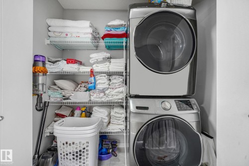 Dedicated laundry area featuring a stacked washer and dryer unit, integrated shelving system, ample storage capacity, and light gray wall paint - 17724 58 Street Nw, Edmonton, AB 