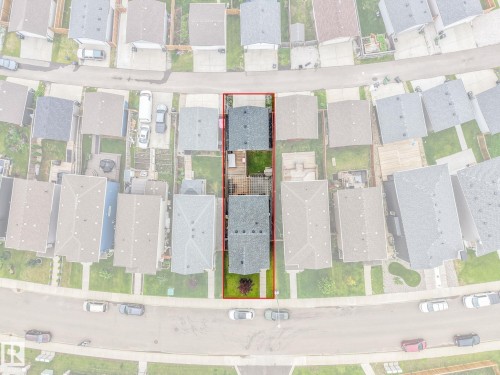 Aerial view showcasing the property with a red border, featuring a main residential structure, a paved patio area, and a green lawn - 17724 58 Street Nw, Edmonton, AB 
