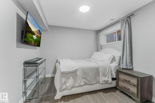 Bedroom featuring light gray walls, wood-finish flooring, a white window trim, and a ceiling-mounted light fixture - 17724 58 Street Nw, Edmonton, AB 