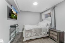 Bedroom featuring light gray walls, wood-finish flooring, a white window trim, and a ceiling-mounted light fixture - 
