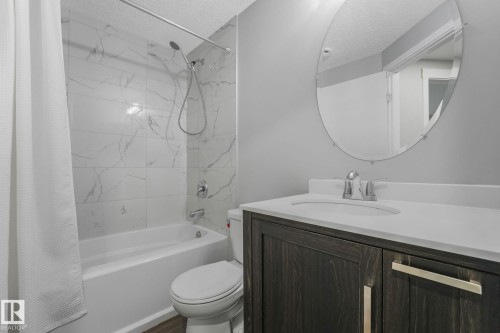 Bathroom featuring a white bathtub with a tile surround, a single vanity with a white countertop, dark wood-finish cabinetry, and an oval mirror - 17724 58 Street Nw, Edmonton, AB 