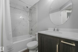 Bathroom featuring a white bathtub with a tile surround, a single vanity with a white countertop, dark wood-finish cabinetry, and an oval mirror - 