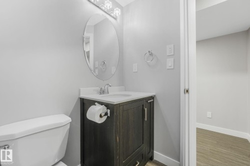 Bathroom featuring a dark wood-finish vanity with a white countertop and oval mirror, complemented by a modern light fixture - 17724 58 Street Nw, Edmonton, AB 