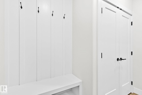 Built-in mudroom bench with vertical paneling and four black coat hooks - 204 Falcon Crescent, Leduc, AB 