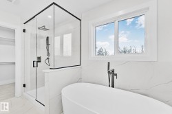 Modern bathroom featuring a freestanding soaking tub with floor-mounted faucet, a glass-enclosed shower with black hardware and a rain showerhead, and marble-look wall tiles - 
