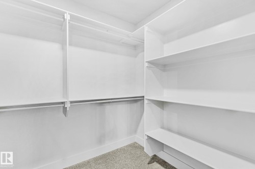 Walk-in closet featuring white built-in shelving, multiple hanging rods, and light gray carpeting - 204 Falcon Crescent, Leduc, AB 