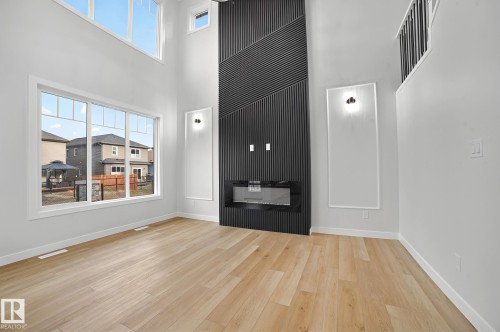 Expansive living space featuring a floor-to-ceiling accent wall with an integrated electric fireplace, wood-finish flooring, and large windows - 204 Falcon Crescent, Leduc, AB 