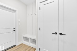 Entryway featuring wood-finish flooring, a built-in bench with storage cubbies, vertical paneling with coat hooks, and solid white doors with matte black hardware - 