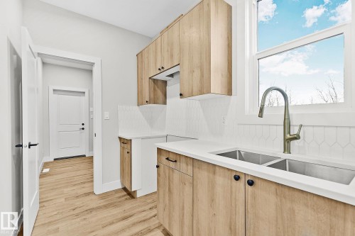 Contemporary kitchen featuring wood-finish cabinetry with matte black hardware, white countertops, and a full-height geometric tile backsplash - 204 Falcon Crescent, Leduc, AB 
