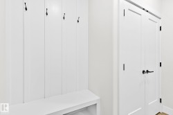 Built-in mudroom bench with vertical paneling and four black coat hooks - 