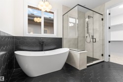 Freestanding soaking tub, walk-in shower with glass enclosure, hexagonal floor tile, black fixtures, and a modern globe chandelier - 