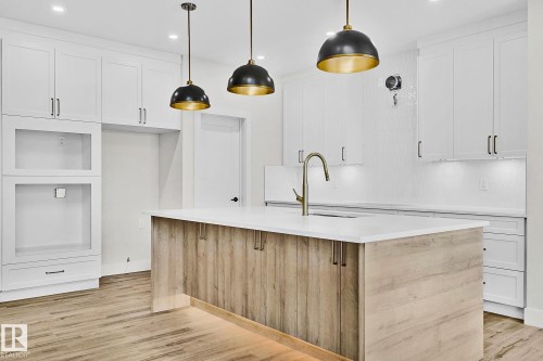 Modern kitchen island with wood-finish paneling, white countertop, and integrated sink with a brass-finish gooseneck faucet - 204 Falcon Crescent, Leduc, AB 