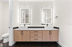 Dual vessel sinks with wall-mounted faucets, illuminated vanity mirrors, floating wood-finish vanity with drawer storage, and hexagonal floor tiling - 