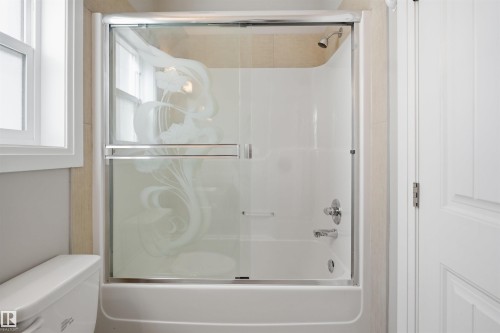 Bathtub and shower combination featuring a sliding glass enclosure with etched design, chrome fixtures, and light-toned tile surround - 16807 54 Street, Edmonton, AB - Indoor Photo Showing Bathroom