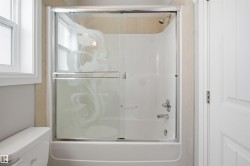 Bathtub and shower combination featuring a sliding glass enclosure with etched design, chrome fixtures, and light-toned tile surround - 