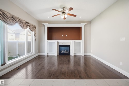 Living area featuring a gas fireplace with a stone surround, built-in shelving, wood-finish flooring, a ceiling fan, and large windows - 16807 54 Street, Edmonton, AB - Indoor With Fireplace