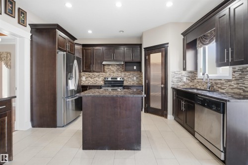 Kitchen featuring dark wood cabinetry, a central island, stainless steel appliances, a tiled backsplash, and light-toned tile flooring - 16807 54 Street, Edmonton, AB - Indoor Photo Showing Kitchen With Stainless Steel Kitchen With Upgraded Kitchen