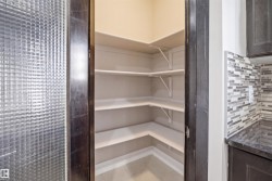 Walk-in pantry featuring corner shelving, light-toned walls, and tile flooring - 