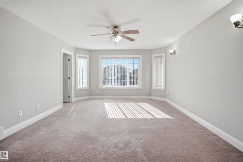Expansive carpeted room featuring a bay window with vertical blinds, a ceiling fan with integrated lighting, and two wall-mounted sconces - 16807 54 Street, Edmonton, AB - Indoor Photo Showing Other Room