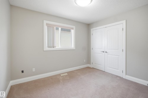 Carpeted room featuring a double-pane window, flush-mount ceiling light, white trim, and a double-door closet with polished chrome hardware - 16807 54 Street, Edmonton, AB - Indoor Photo Showing Other Room