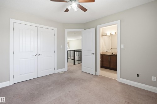 Carpeted room featuring a ceiling fan with light fixture, double-door closet with arch-top panels, and an open doorway revealing a vanity with a dark wood-finish cabinet and wall-mounted light fixture - 16807 54 Street, Edmonton, AB - Indoor Photo Showing Other Room
