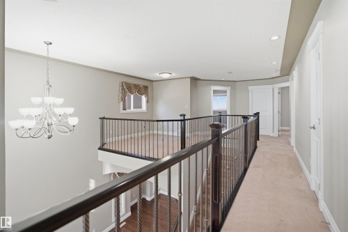 Second-story landing featuring a chandelier, carpeted hallway, dark wood-finish handrails with wrought iron balusters, recessed lighting, and white trim - 16807 54 Street, Edmonton, AB - Indoor Photo Showing Other Room