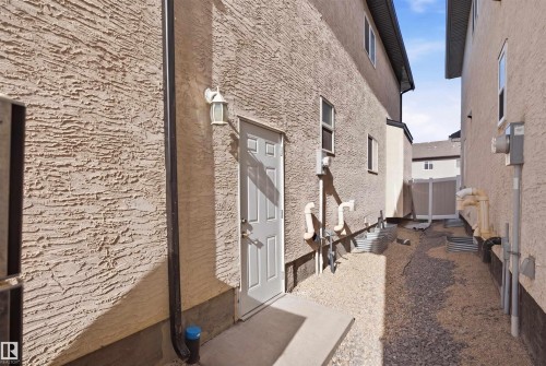 Exterior wall with a textured stucco finish and a white side entry door featuring a decorative outdoor lantern - 16807 54 Street, Edmonton, AB - Outdoor With Exterior