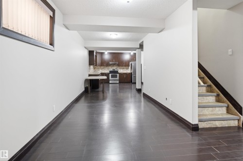 Open-concept living area featuring dark wood-finish flooring, a contemporary kitchen with dark cabinetry and stainless steel appliances, and a staircase with patterned tile risers - 16807 54 Street, Edmonton, AB - Indoor