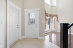 Foyer with decorative leaded glass front door, tile flooring, rich wood-finish flooring, and a dark wood banister - 