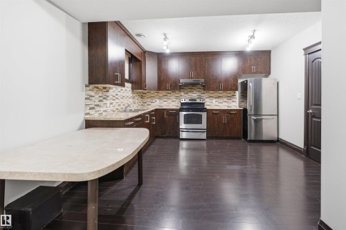 Kitchen featuring dark wood-finish cabinetry, stainless steel appliances, mosaic tile backsplash, and a light-toned countertop - 16807 54 Street, Edmonton, AB - Indoor Photo Showing Kitchen With Stainless Steel Kitchen With Upgraded Kitchen