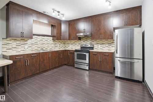 Kitchen featuring wood-finish cabinetry with silver hardware, light-toned countertops, and a tiled backsplash - 16807 54 Street, Edmonton, AB - Indoor Photo Showing Kitchen With Stainless Steel Kitchen With Upgraded Kitchen