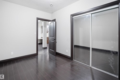 Rich wood-finish flooring complemented by dark trim throughout, a contemporary interior door with vertical paneling, and sliding mirrored closet doors - 16807 54 Street, Edmonton, AB - Indoor Photo Showing Other Room
