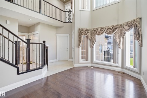 Two-story entry foyer featuring dark wood-finish flooring, a grand staircase with wrought iron balusters, and a bay window configuration with upper transom windows - 16807 54 Street, Edmonton, AB - Indoor Photo Showing Other Room