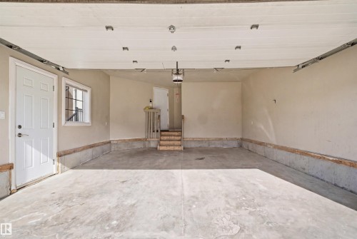 Spacious garage featuring a concrete floor, painted walls, a side entry door, a window with grilles, and interior access via a wooden staircase - 16807 54 Street, Edmonton, AB - Indoor Photo Showing Garage