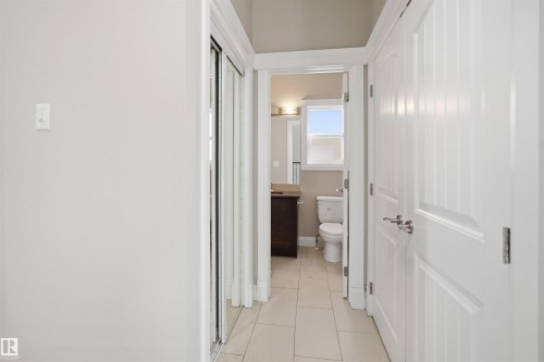 Hallway featuring white panel doors, mirrored closet doors, and light-toned tile flooring - 16807 54 Street, Edmonton, AB - Indoor