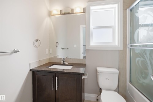 Contemporary bathroom featuring a dark wood-finish vanity with an integrated sink, polished chrome fixtures, and a large wall-mounted mirror - 16807 54 Street, Edmonton, AB - Indoor Photo Showing Bathroom