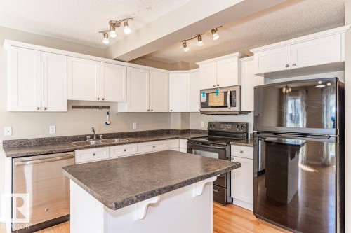 Kitchen featuring white cabinetry, dark countertops, a central island, stainless steel dishwasher, and track lighting - 39 Vega Avenue, Spruce Grove, AB - Indoor Photo Showing Kitchen With Double Sink
