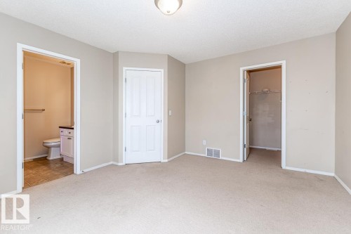 Neutral-toned carpeting extends throughout this room, featuring an open doorway revealing a bathroom with tile flooring, a white vanity with dark countertop, and a toilet - 39 Vega Avenue, Spruce Grove, AB - Indoor