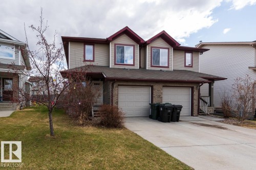 Duplex property featuring a two-car garage with individual doors, a light-colored siding facade, and contrasting maroon trim - 39 Vega Avenue, Spruce Grove, AB - Outdoor
